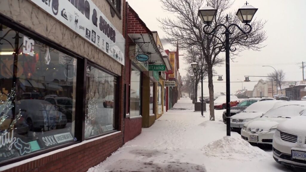 Exterior shot of shops along main street Osoyoos, with snow covering the sidewalks and parked cars. 