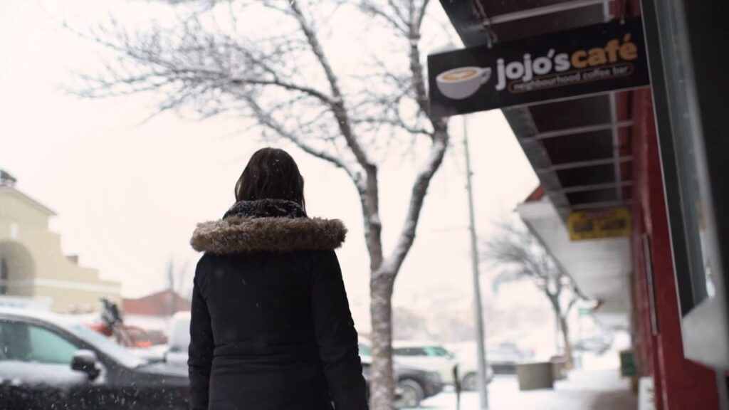 Photo of a person walking down a snowy main street with a sign for JoJo's Cafe beside them