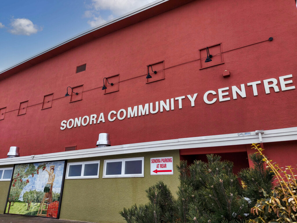 The red and sage green front of the Sonora Community Centre with the mosaic mural out front.  