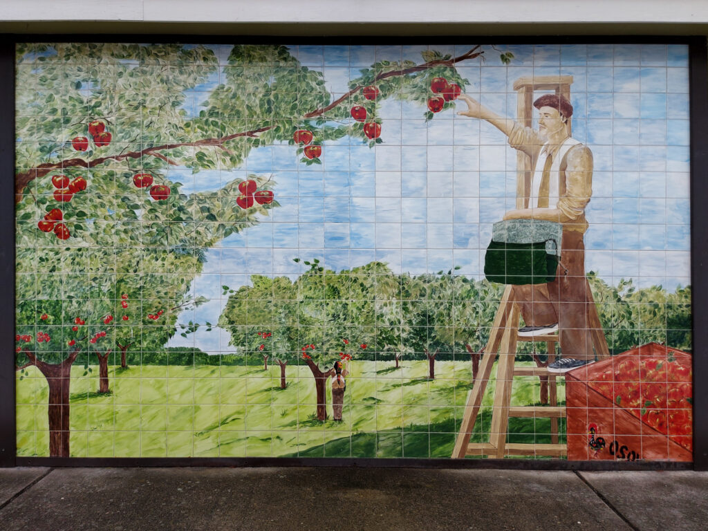 A close up of the mosaic mural featuring a painting of an orchardist picking apples. 