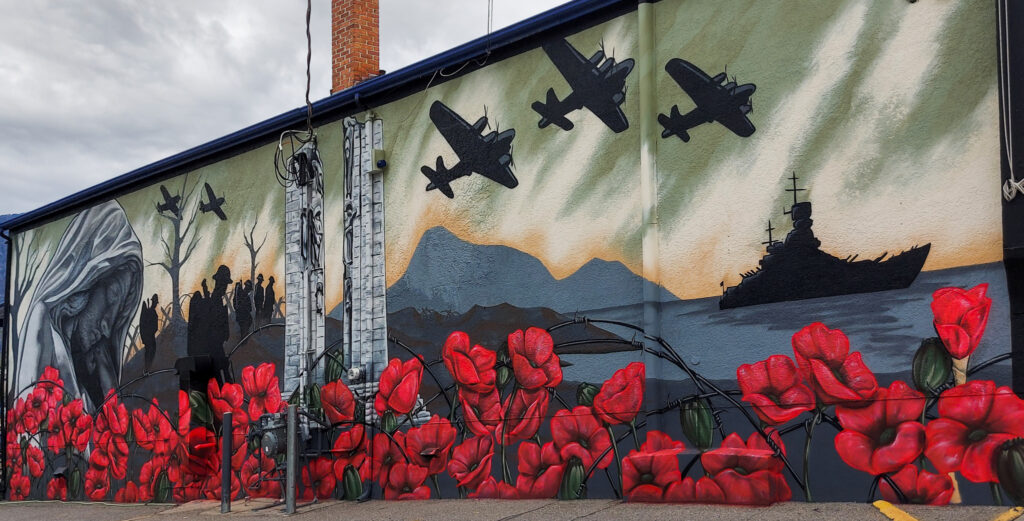 Side of the Osoyoos Legion Hall with mural featuring poppies and silhouettes of airplanes and soldiers. 